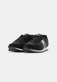 Zwarte sportschoenen met vetersluiting, een gestructureerde bovenkant en een witte rubberen zool. Voorzien van gekleurde strepen in rood, blauw en wit aan de zijkant.