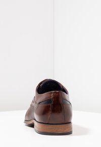 Zapato de cuero marrón con un acabado suave, que presenta un puntera redondeada, detalles en negro contrastantes y un tacón de madera.
