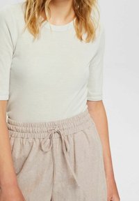 Světle béžový vroubkovaný top s krátkými rukávy spárovaný se světle béžovými kalhotami na elastický pas se zavazováním. Měkká textura a ležérní design.