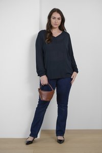 Svart blus med lång ärm och V-ringning, kombinerad med mörkblå jeans. Håller en liten brun läderhandväska. Svarta spetsiga klackskor.