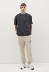 Dunkelgraues T-Shirt mit kurzen Ärmeln und rundem Ausschnitt, kombiniert mit beigen Cargo-Hosen mit seitlichen Taschen und elastischen Bündchen.