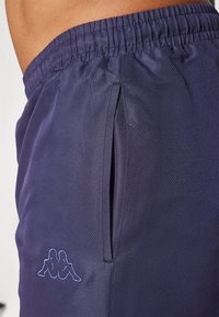 Shorts décoratifs de couleur marine avec un motif texturé, taille élastique, poches latérales et un logo brodé bleu clair près de l'ourlet.