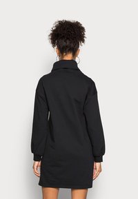 Robe sweat-shirt noire oversize avec col montant, manches longues bouffantes et ourlets retroussés. Tissu doux avec une texture lisse.