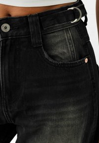 Czarne dżinsy o wyblakłej fakturze, z metalowym guzikiem, szlufkami na pasek oraz widocznymi detalami kieszeni.