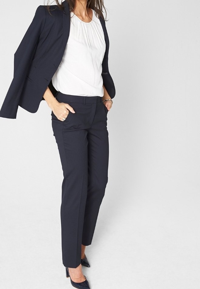 Navy Blazer mit strukturierten Schultern, weißer plissierter Bluse und schmal geschnittenen navy Hosen. Zusätzliche Details sind spitze High Heels und ein Armband.