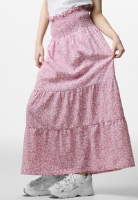 Roze, bloemenpatroon maxi rok met een geschuurd tailleband en gelaagde fronsen, gecombineerd met lichtgekleurde sneakers.
