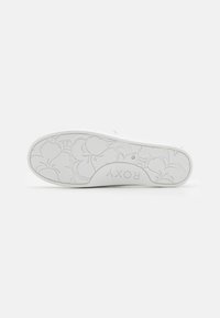 Sola di sneakers bianche con motivo floreale e nome del marchio "ROXY" impresso al centro, su uno sfondo bianco uniforme.
