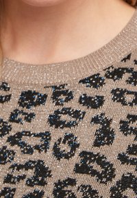 Pull en tricot beige avec un imprimé léopard noir et bleu, doté d'une texture légèrement pailletée. Il a une encolure ronde.