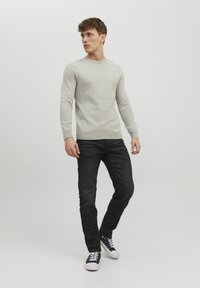 Suéter texturizado gris claro, ajuste ceñido, cuello redondo, combinado con jeans oscuros y zapatillas negras con suelas blancas.