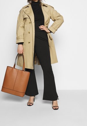 Beige trenchcoat met gouden knopen, zwart ribbeltop, zwarte flared pants, bruine leren totebag en zwarte haksandalen.