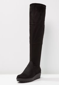 Svart över knästövel i mjukt, slätt material med kilklack. Har en rundad tå och sömdetaljer på skafte.