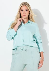Lyseblågrøn skjorte med knapper og lange ærmer, lavet af blødt stof, kombineret med matchende bukser med snøre i en lignende nuance.