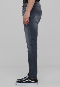Slim-fit tummat denim farkut, joissa on haalistunut pinta ja pieni kuluma polvessa. Yhdistetty mustiin ja valkoisiin matalakampaisiin lenkkareihin.