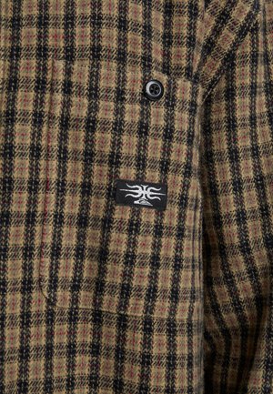 Wollen jas met een bruin en zwart geruit patroon, voorzien van rode accenten, een zwarte knop en een logo-opdruk aan de linkerkant.