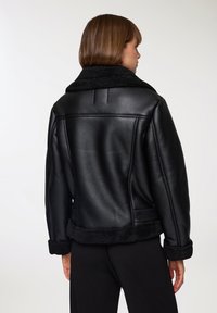 Giacca in pelle nera con colletto e polsini in shearling, caratterizzata da una texture liscia, un design strutturato e accenti in tessuto morbido a contrasto.