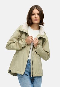 Lys grønn hettejakke med glidelås, elastiske mansjetter og myk kremfargefôr. Har sidelommer og et logopatch på kanten.