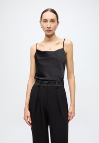 Črna satenasta majica s tankimi naramnicami, združena z visokim pasom črnih hlač z satenastim pasom. Enostavna, elegantna silhueta.