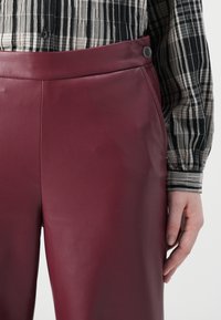 Bordeaux faux leren broek met een gladde textuur, hoge taille en een zwarte knoopsluiting. Gestyled met een zwart-wit gestreepte blouse.