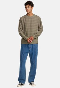 Grüner Pullover mit langen Ärmeln und horizontalen Streifen. Aus einem Baumwollmischmaterial, mit Rundhalsausschnitt gestaltet, kombiniert mit blauen, weit geschnittenen Jeans und schwarzen Sneakers.