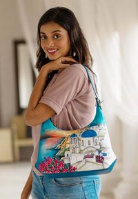 Hobo tas met een blauwe achtergrond en een schilderachtig beeld van witte gebouwen en blauwe koepels, verfraaid met roze bloemen. Zachte textuur.