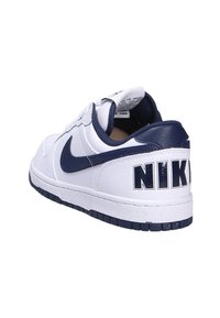 Baskets en cuir blanc avec des accents bleu marine, comportant un logo Nike bien visible sur le talon, une semelle en caoutchouc plate et une tige texturée.