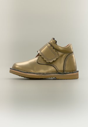Chaussure enfant en cuir doré métallisé avec bride Velcro à bord festonné et semelle en caoutchouc, vue de profil sur fond neutre.