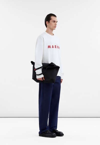 Sweatshirt blanc avec texte "MARNI" rouge, pantalon bleu marine, sac noir avec poignées, et chaussures noires avec semelle texturée. Design simple et moderne.