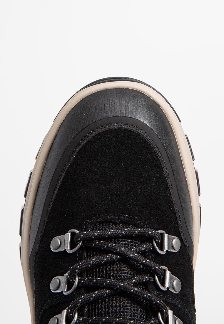 Chaussure de randonnée noire en suédine et matériaux synthétiques, avec un dessus noir texturé, des œillets métalliques et une semelle beige durable.