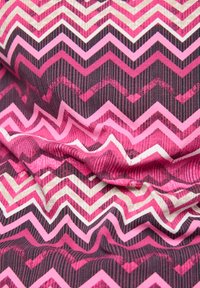 Textil mit einem Zickzackmuster in Rosa-, Weiß- und Schwarztönen, das unterschiedliche Streifen und einen weichen, strukturierten Stoff aufweist.