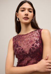 Bordó csipke felső flitterekkel. Áttetsző anyag, ujjatlan kialakítás, kerek nyakkivágás. Finom virágmintával, amely kiemeli a textúrát és a csillogást.