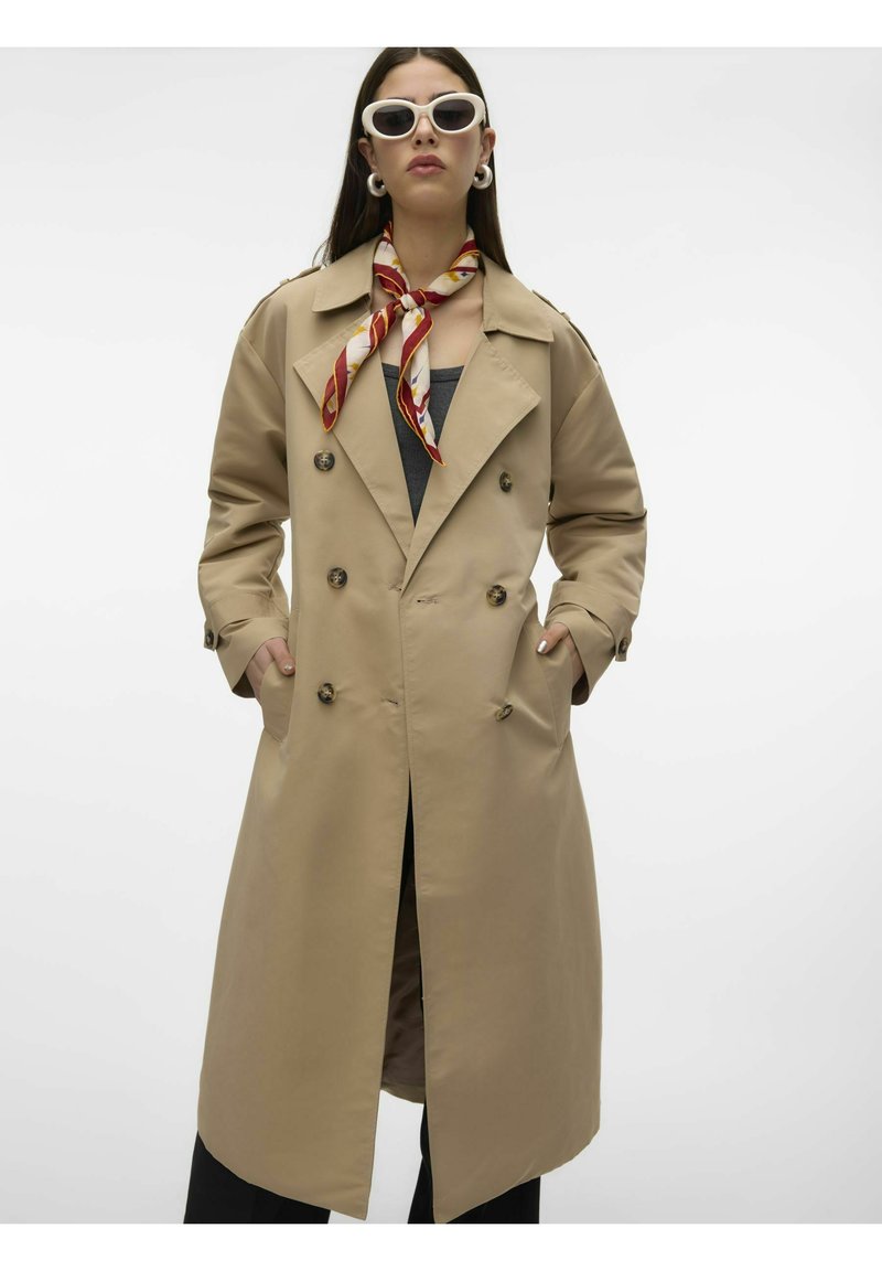 Beige dobbeltradet trenchcoat med store knapper, sidelommer og en ryggslisse. Har en bred krage og glatt tekstur.