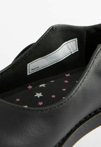 L'intérieur de la chaussure noire présente une texture lisse, avec une semelle intérieure amovible affichant un motif d'étoiles en violet et argent sur un fond noir.