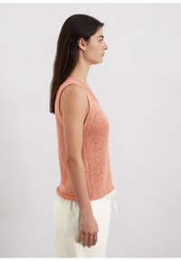 Mouwloze perzikkleurige gebreide top met een gestructureerde afwerking en V-hals, gecombineerd met lichtgekleurde joggingbroek met trekkoord. Eenvoudig ontwerp en casual pasvorm.