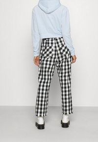 Cropped hoodie blu chiaro abbinato a pantaloni a vita alta check bianco e nero, con tasche frontali e orli sfrangiati, indossato con stivali bianchi.