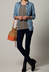 Camicia di jeans, top grigio a righe con bottoni, jeans skinny scuri, stivali neri alla caviglia e una borsa a tracolla beige con dettagli arancioni.