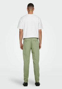 Conjunto de hombre que incluye una camiseta blanca de cuello redondo y pantalones relajados de color verde claro con dos bolsillos traseros, combinados con zapatos negros.