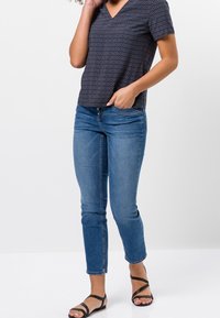 Top de pico de patrón azul marino combinado con jeans ajustados de color azul. El top tiene mangas cortas, mientras que los jeans son de tiro medio y con los tobillos acortados. Sandalias negras.