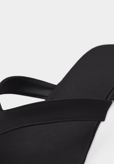 Μαύρο σανδάλι με έναν φαρδύ λουρί πάνω από το πόδι και ελαφρώς ανυψωμένη σόλα σε λευκό φόντο.