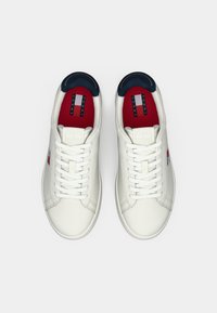 Witte leren sneakers met een zachte afwerking, voorzien van marineblauwe accenten op de kraag en een rode binnenzool met een Tommy Jeans-logo.