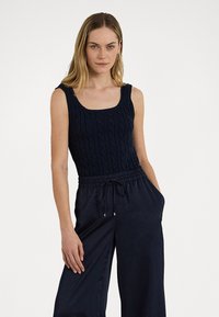 Débardeur en tricot bleu marine avec un décolleté carré, présentant un motif de tricot en câble. Associe avec un pantalon ample à cordon assorti.