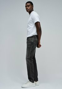 Jeans de mezclilla negra con un corte recto, combinados con una camiseta blanca lisa y zapatillas blancas. La tela muestra un ligero desvanecimiento.