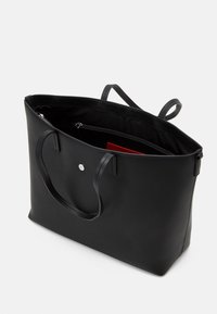 Czarna torba typu tote wykonana z gładkiego materiału, wyposażona w dwie rączki, zapięcie na zamek oraz kieszeń wewnętrzną. Charakterystyczne srebrne okucia.