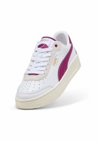 Zapatillas blancas de cuero con una franja lateral morada, puntera perforada y una suela gruesa de color crema. Cuentan con cordones y un logo.
