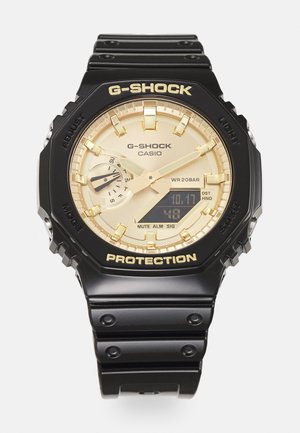 G-Shock-kello, jossa on musta hartsihihna, kultasävyinen analoginen ja digitaalinen kellotaulu, teksturoitu kehys sekä erottuvat "PROTECTION" ja "G-SHOCK" -merkit.