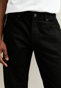 Jeans de mezclilla negra con corte recto, que presentan un cierre de botón, bolsillos delanteros y una tela texturizada sutil.