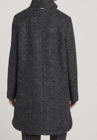 Cappotto in misto lana di colore grigio scuro, con collo alto, maniche lunghe e taglio dritto. Sul retro presenta una cucitura centrale e un dettaglio discreto del logo.