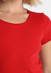 Czerwony bawełniany t-shirt z okrągłym dekoltem i krótkimi rękawami. Posiada małe haftowane logo po lewej stronie na klatce piersiowej. Miękka tekstura, dopasowany krój.