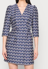 Granatowa sukienka z dekoltem w kształcie litery V i rękawami o długości trzy czwarte, z falistym wzorem w białe i czerwone paski oraz dopasowanym talią.