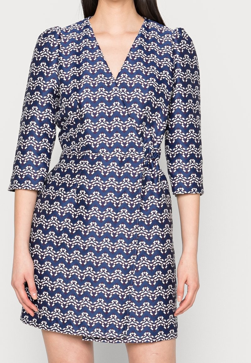 Granatowa sukienka z dekoltem w kształcie litery V i rękawami o długości trzy czwarte, z falistym wzorem w białe i czerwone paski oraz dopasowanym talią.