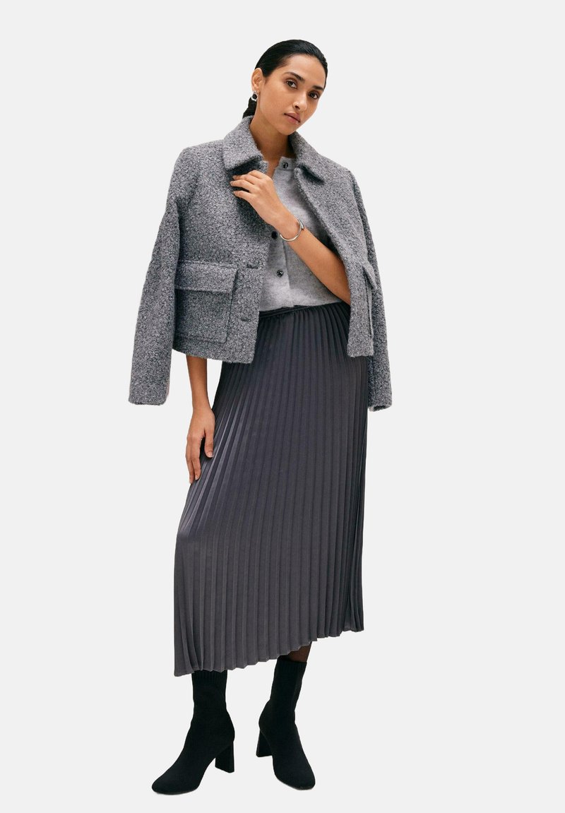 Grijze twijde blazer met een kraag, grijze trui eronder en een geplooide donkergrijze rok. Afgerond met zwarte leren enkellaarsjes met hak.
